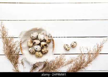 Mucchio di uova di quaglia in legno naturale ciotola interno su sfondo bianco tavola di legno. Sopra la vista, molto spazio di copia. Foto Stock