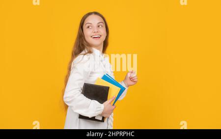 ragazza teen stupita in esecuzione con libro di lavoro della scuola su sfondo giallo, spazio di copia, infanzia Foto Stock