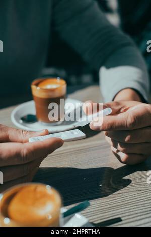 primo piano di un giovane uomo caucasico, seduto ad un tavolo di un caffè marciapiede, mettendo il suo campione nel dispositivo di test diagnostico dell'antigene covid-19 Foto Stock