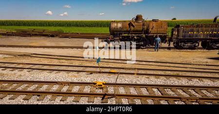 Strasburg, Pennsylvania, luglio 2019 - Vista di un ingegnere in piedi accanto ad un vecchio motore a vapore di dorso di cammello Rusty che è stato Striped del suo Cab in un giorno di sole Foto Stock