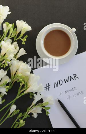 Nessun messaggio di guerra su carta bianca, tazza di caffè e fiori bianchi su sfondo scuro. Spazio di copia Foto Stock