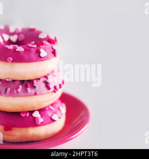 Su un piccolo piattino rosso sono tre ciambelle dolci rosa deliziosa con spolverini colorati. Bellissimo dessert. Prodotti da forno. Cibo spazzatura. Foto Stock