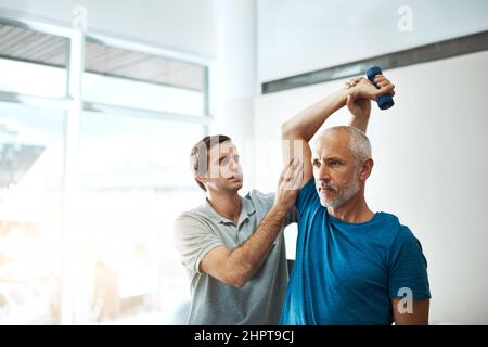 Questi esercizi sono molto importanti per il vostro recupero. Shot di un giovane fisioterapista maschile che aiuta un cliente con esercizi di stretching nel suo ufficio Foto Stock