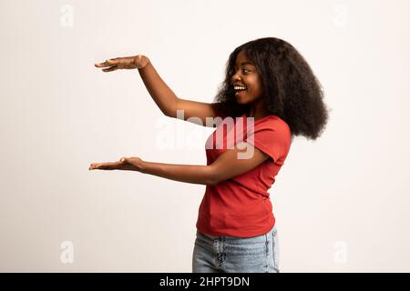 Eccitata Black Female che tiene in mano un grande oggetto invisibile Foto Stock