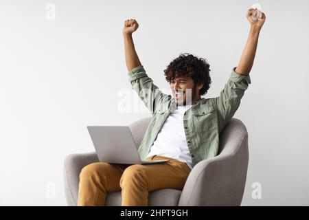 Uomo indiano felice con il portatile che solleva le mani Foto Stock