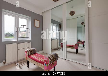 Lo spogliatoio si riflette in una grande porta a specchio che dà l'impressione di uno spazio più grande con interessante sgabello rosa e decorato in grigio e bianco Foto Stock