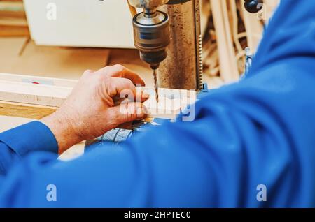 Foratura su tavola di legno. Realizzazione di gambe in legno per cavalletti. Lavori di Falegnameria. Mani di maestro in alto da vicino. Foto Stock