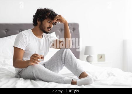 Frustrato ragazzo indiano che beve alcol, seduta a letto, spazio copia Foto Stock