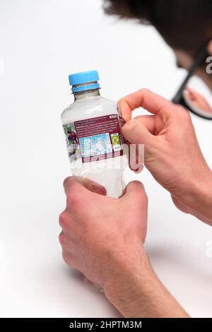 Rimozione dell'etichetta per il riciclaggio su una bottiglia di plastica monouso, la bottiglia ha un'etichetta Ribena e viene fotografata su sfondo bianco. Foto Stock