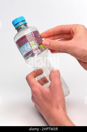 Rimozione dell'etichetta per il riciclaggio su una bottiglia di plastica monouso, la bottiglia ha un'etichetta Ribena e viene fotografata su sfondo bianco. Foto Stock