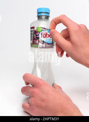 Rimozione dell'etichetta per il riciclaggio su una bottiglia di plastica monouso, la bottiglia ha un'etichetta Ribena e viene fotografata su sfondo bianco. Foto Stock