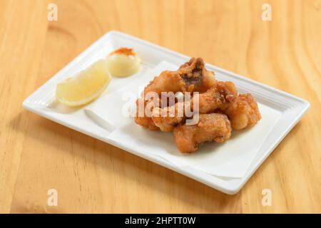 Cibo giapponese fritto Tako Karaage con limone in un piatto bianco isolato sul tavolo di legno vista dall'alto Foto Stock