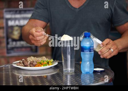 Un bodybuilder che aggiunge supplementi alla sua acqua mentre mangiano un pasto proteico-pesante. Un bodybuilder che aggiunge supplementi alla sua acqua mentre mangia una proteina Foto Stock