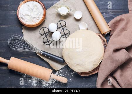 Pasta cruda con farina, uova e utensili su sfondo di legno Foto Stock