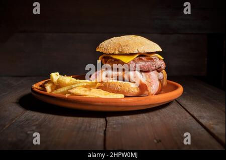 Hamburger di manzo alla griglia di prima qualità con pancetta, formaggio e patatine fritte. Delizioso hamburger americano su sfondo di legno. Fotografia di alta qualità Foto Stock