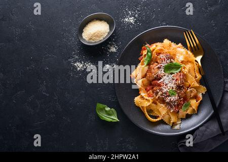 Tagliatelle con polpette di pomodoro, basilico e parmigiano su fondo di pietra nera o cemento. Piatti italiani e cucina tradizionale Foto Stock