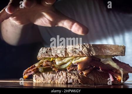 Sandwich di pastrami su una tavoletta di legno con delizioso incontro sul pane baguette con formaggio, spazio copia in parti dell'immagine. Foto Stock