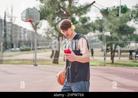 giovane atleta che si allena in campo di pallacanestro mentre ascolta la musica. Foto Stock