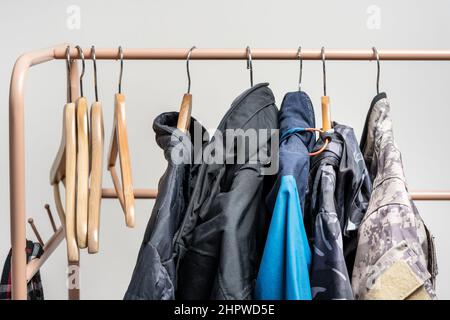 diversi appendiabiti in legno vuoti appesi in un bar insieme ad altri con abiti caldi di vari colori Foto Stock