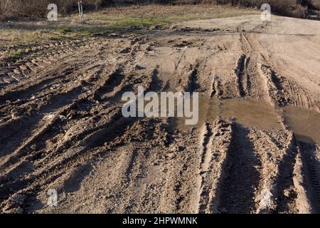 Strada sterrata di campagna in montagna con un sacco di pozzanghere fangose dopo la pioggia in una giornata di primavera soleggiata Foto Stock