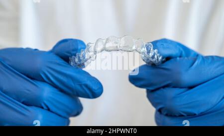 Mano maschio in guanti che tengono fermo allineatore dentale su sfondo bianco della clinica dentale per un bel trattamento dei denti. Diritto ortodontico rimovibile Foto Stock