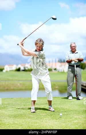 Ha perfezionato la sua oscillazione nel corso degli anni. Immagine di una donna matura in pieno swing durante un gioco di golf con suo marito. Foto Stock