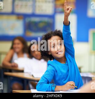 Pick me conosco la risposta. Un ragazzino che alza la mano in classe. Foto Stock