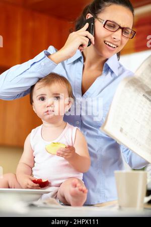 Im sensazione un po 'lasciato fuori. Scatto di una mamma singola frustrata che alimenta il suo bambino mentre cerca di parlare al telefono e tenere un giornale. Foto Stock