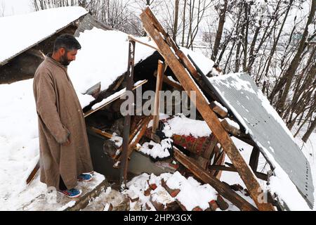 Budgam, India. 22nd Feb 2022. Un proprietario di casa ispeziona la sua casa danneggiata a Bugam Chadoora villaggio. La valle del Kashmir ha ricevuto pesanti nevicate che hanno portato alla chiusura di strade in zone lontane oltre al ritardo di diversi voli che operavano dall'aeroporto di Srinagar. Anche i servizi ferroviari locali sono stati sospesi. Credit: SOPA Images Limited/Alamy Live News Foto Stock