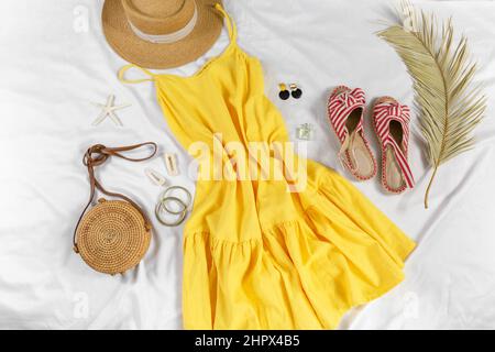 Cappello di paglia, abito giallo, borsa di paglia su sfondo bianco. Outfit estivo alla moda. Stay piatto con vestiti per vacanze e vacanze. Foto Stock
