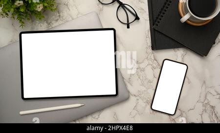 Moderna scrivania da ufficio, vista dall'alto, piatto con tablet digitale e mockup per smartphone con schermo bianco, forniture per ufficio e caffè su sfondo marmo. Foto Stock