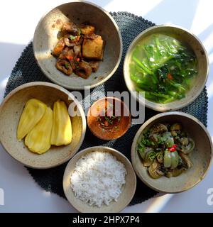 Vassoio con vista dall'alto di cibo vegano vietnamita, ciotola di riso, melanzane fritte, cuoco di seitan con salsa, zuppa di spinaci, menu dietetico non a base di carne per il pasto di famiglia quotidiano Foto Stock