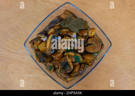 Un piatto di vetro con funghi sottaceto si trova su un asse di legno. Foto Stock