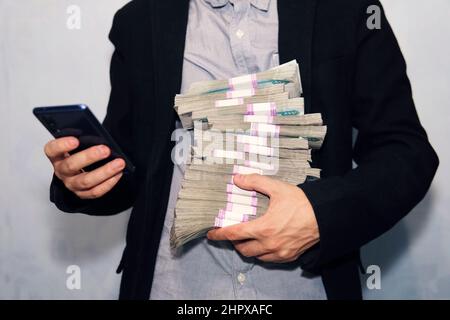 Smartphone e denaro. Il giovane è in possesso di uno smartphone e una grande bacchetta di 1000 rubli fatture. Guadagni con l'aiuto del telefono. Foto Stock