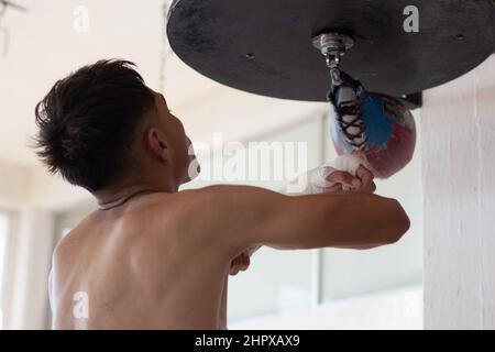 pugile leggero allenarsi la sua velocità e coordinazione punzonando il sacco di boxe con le mani fasciate Foto Stock