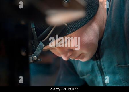 Ritratto di un saldatore ad arco in argon con un faro sulla testa sul posto di lavoro Foto Stock