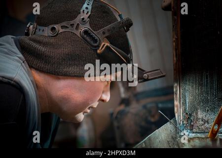 Ritratto di un saldatore ad arco in argon con un faro sulla testa sul posto di lavoro Foto Stock