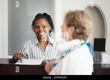 Assistenza diligente e cordiale. Una receptionist che dà ad una donna anziana le chiavi della sua camera d'albergo. Foto Stock