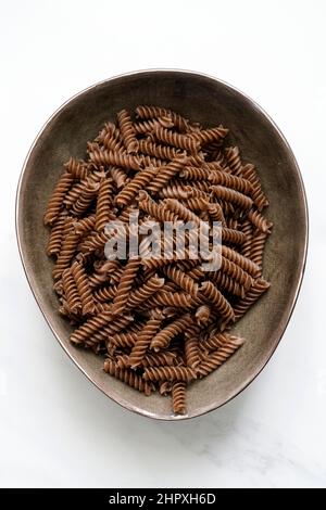 Pasta di farina integrale cruda di grano saraceno da coltivazione biologica, fondo in marmo bianco con spazio per il testo, Italia Foto Stock