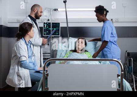 Donna con malattia collegata alla linea di infusione iv e monitor che mostra segni vitali che ricevono cure mediche da infermiere. Il team di medici si occupa della consultazione clinica del paziente con cannula nasale che si recupera dall'intervento chirurgico. Foto Stock