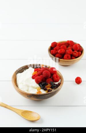 Ciotola di legno di yogurt greco panna montata con lamponi e frutta secca, primo piano su sfondo bianco Foto Stock