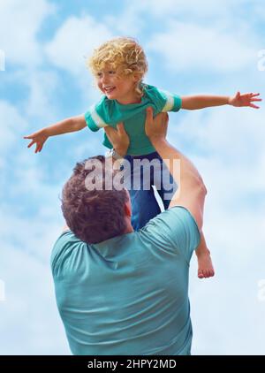 Osare sognare. Un padre che oscilla il figlio del bambino in aria contro uno sfondo di cielo. Foto Stock