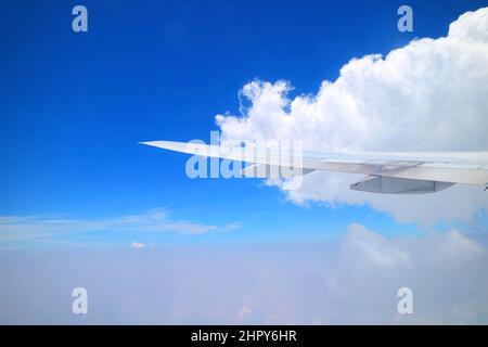 Cielo blu vivo e nuvole bianche con l'ala dell'aeroplano vista dalla finestra dell'aereo durante il volo Foto Stock