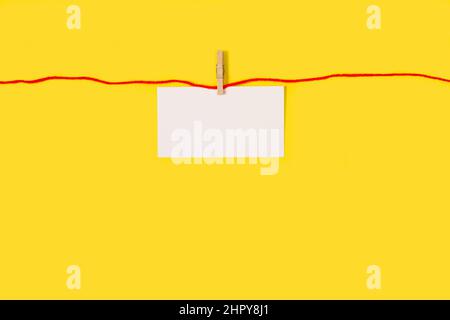 Carta bianca bianca bianca appesa a un filo rosso su sfondo giallo Foto Stock