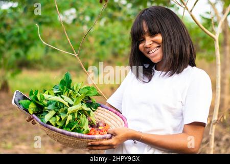 Ritratto di una bella femmina contadina africana che porta cesto di verdure Foto Stock