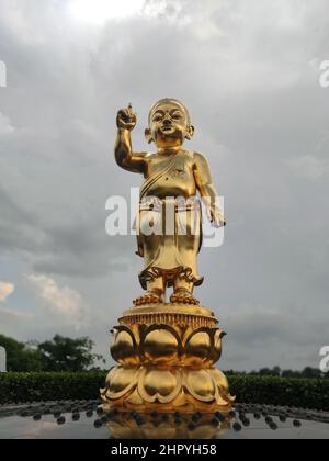 Colpo ad angolo basso della statua dorata del piccolo Buddha contro un cielo nuvoloso a Lumbini, Nepal. Foto Stock