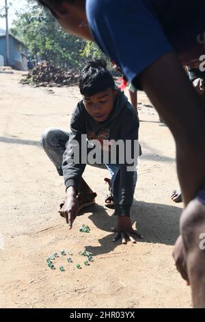 Ragazzo tribale che gioca marmi a Pearson Pally. Il borgo tribale di Santali a Visva-Bharati. Santiniketan, Bolpur, Birbhum, Bengala Occidentale, India. Foto Stock