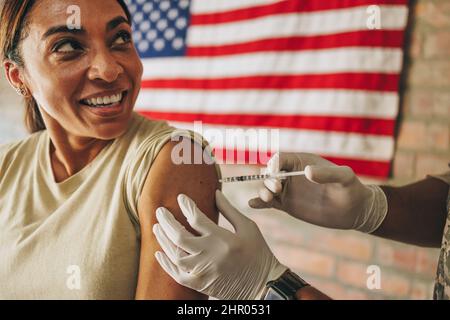 Gli Stati Uniti si inoculano durante la pandemia di coronavirus. Felice soldato femmina sorridente allegro mentre riceve il covid-19 va Foto Stock