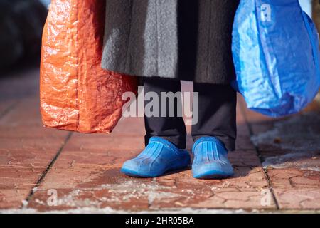 piedi di rifugiati o senzatetto in scarpe sporche a basso costo. Una donna senza volto con grandi borse in mano. Foto Stock