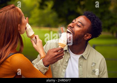 Giovane coppia che viaggia attraverso la città insieme mangiando gelati nel parco Foto Stock